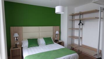 Una habitación de hotel moderna con una pared de acento verde, una cama grande con almohadas verdes, lámparas de noche y un banco de madera.