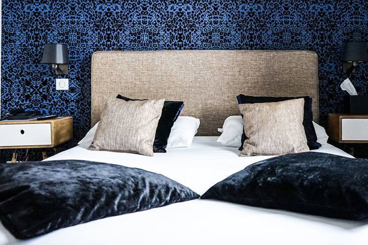 A neatly made bed with a headboard, two bedside tables with lamps, and a patterned wall behind.
