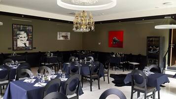 A dining area with round tables, dark blue tablecloths, and modern chandeliers.