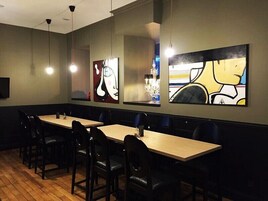 Un restaurante con mesas y sillas largas, obras de arte en las paredes e iluminación colgante.