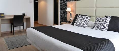A hotel room with a large bed, a desk, and a nightstand with a lamp.