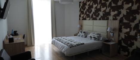 A modern hotel room with a large bed, a desk, a chair, a TV, and a cow print wall.