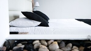 Un lit avec une literie blanche, des oreillers à rayures noires et une télécommande sur le côté.
