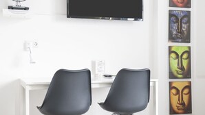 A room with a white desk, two black chairs, a flat-screen TV, and a wall with framed artwork. - NXT PARK Hamburg by ANS (Hamburg)