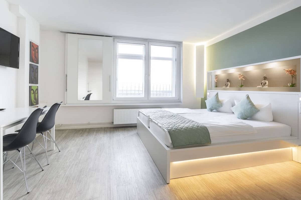 Quarto moderno com cama, mesa de cabeceira e escrivaninha com cadeiras.