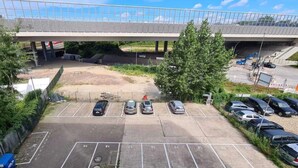 A parking lot with several cars, a pedestrian bridge overhead, and a construction site in the background. - NXT PARK Hamburg by ANS (Hamburg)