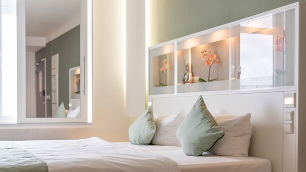 A modern bedroom with a bed, bedside tables, and a large window. - NXT PARK Hamburg by ANS (Hamburg)