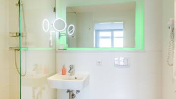 A modern bathroom with a glass shower enclosure, a white sink, a mirror with lights, and a toilet.
