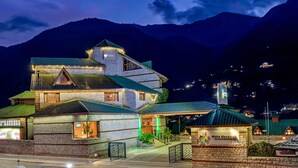 A multi-story hotel with a stone facade, a green roof, and a sign indicating it is part of the White Meadows by Mahindra Holidays. - Club Mahindra White Meadows Manali (Manali)