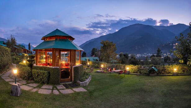 A gazebo with a green roof and glass walls, surrounded by a well-maintained garden with stone pathways and outdoor seating. - Club Mahindra White Meadows Manali (Manali)
