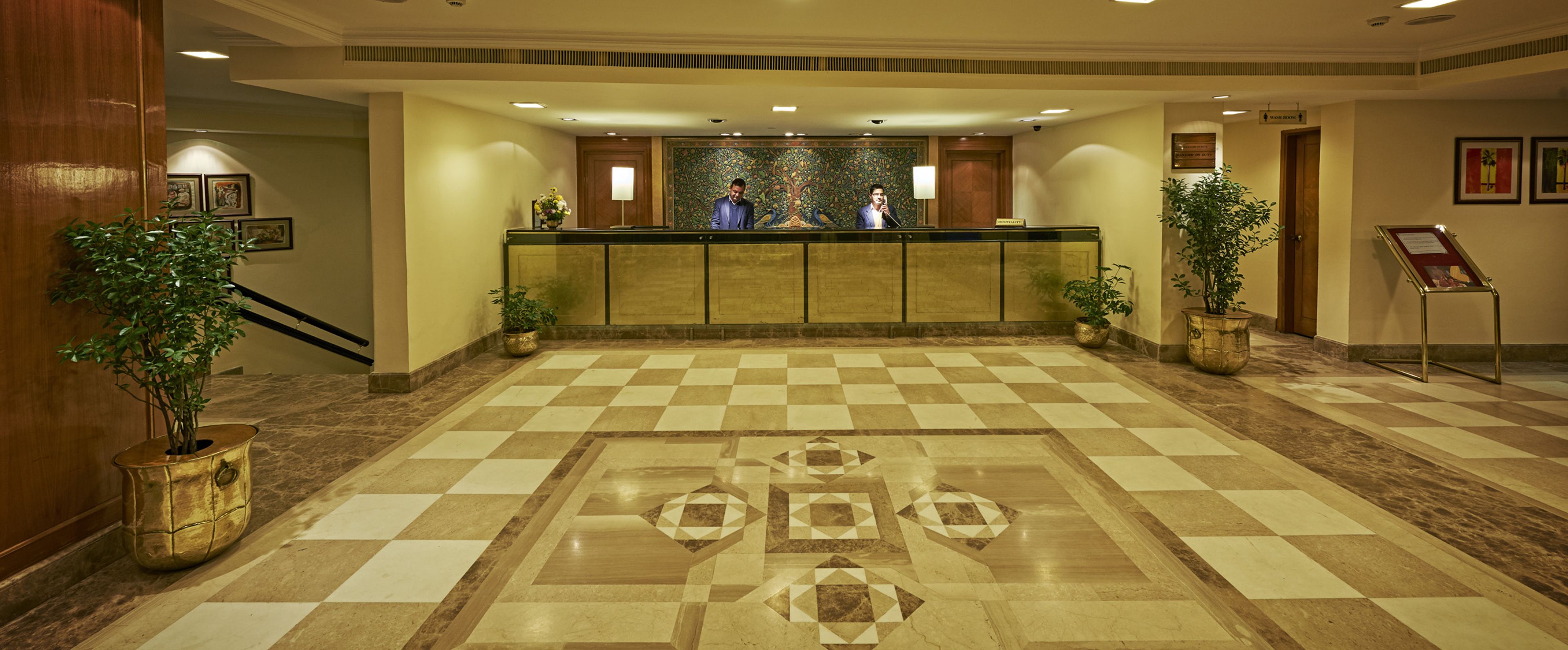 A reception area with a checkered floor, a reception desk, and two potted plants.