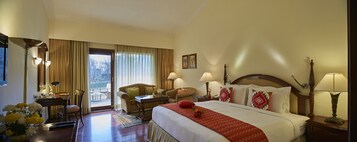 Habitación de hotel con una cama grande, dos sillones, un escritorio y vistas al exterior por la ventana.