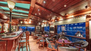 A bar area with wooden furniture, a bar counter, and a view of the city. - Club Mahindra White Meadows Manali (Manali)