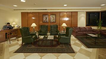 Un hall con mostrador de recepción, sillones de cuero verde, un sofá de cuero marrón y una alfombra estampada.