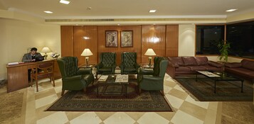 Un hall con mostrador de recepción, sillones de cuero verde, un sofá de cuero marrón y una alfombra estampada.