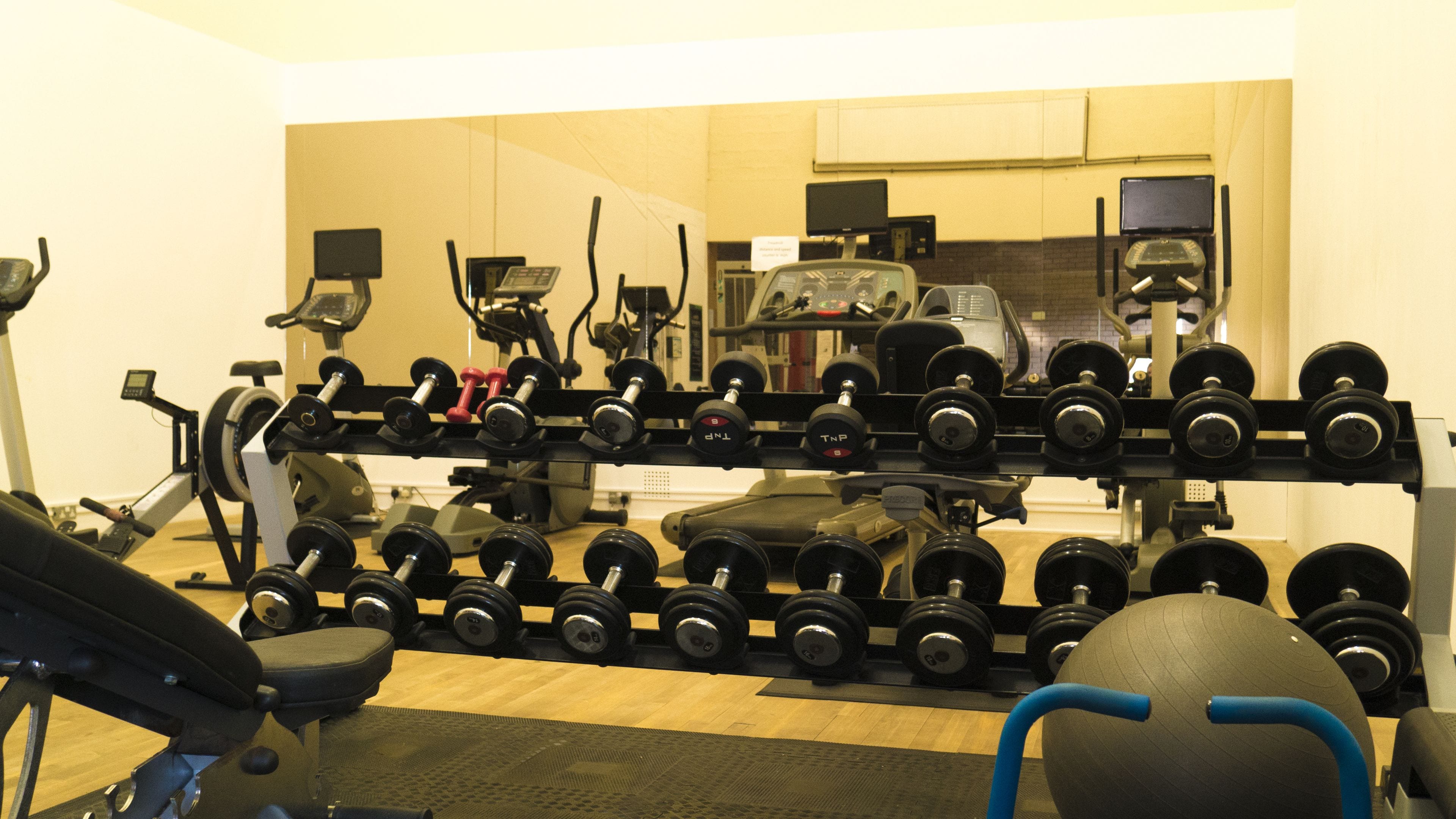A gym with various exercise equipment including dumbbells, treadmills, and stationary bikes.