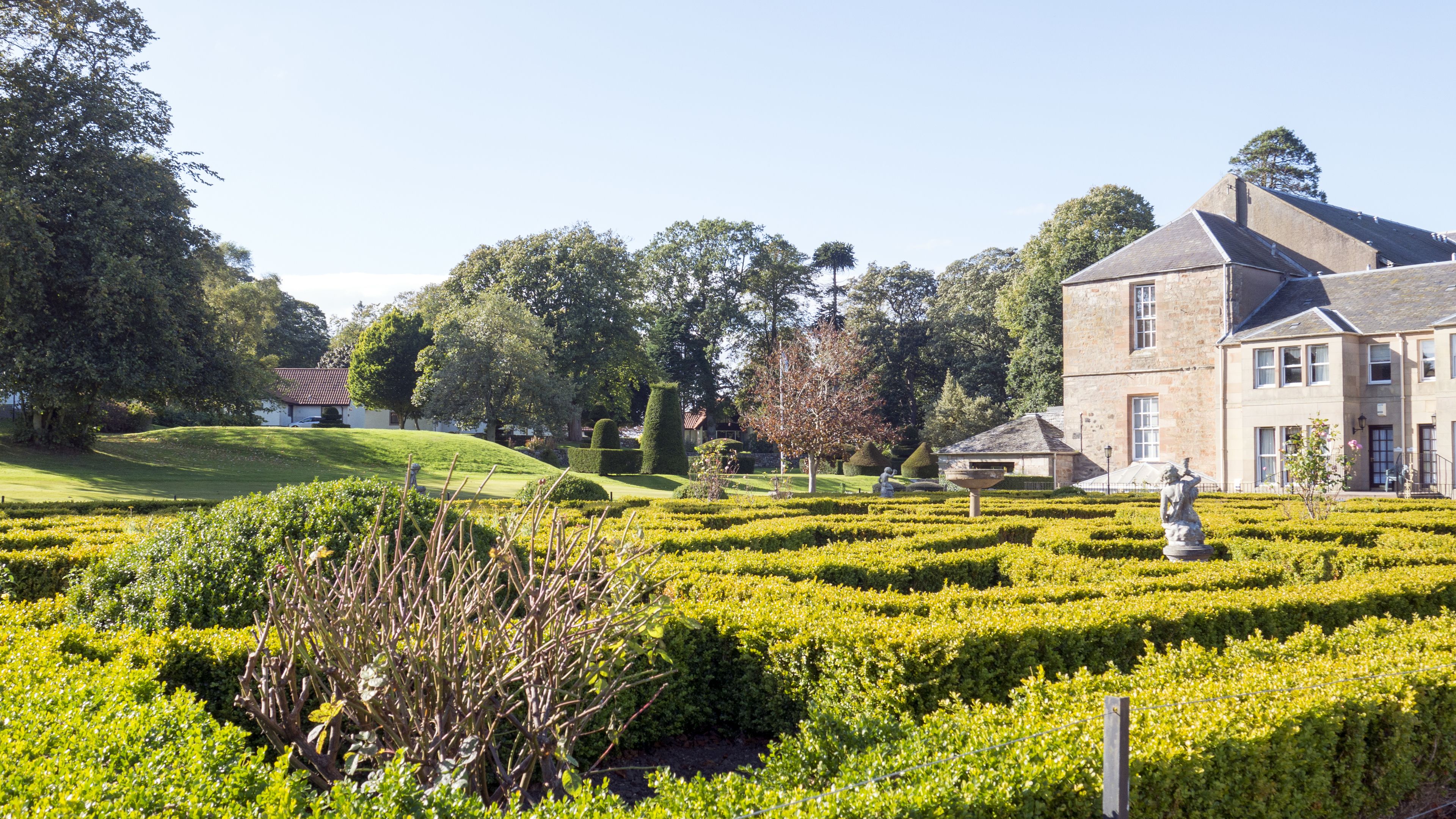 A well-maintained garden with hedges, a statue, and a large stone building with multiple windows.