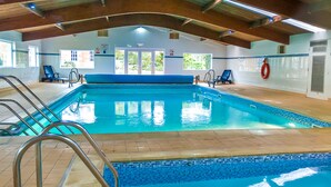 An indoor swimming pool with clear blue water, tiled edges, and a wooden ceiling. - Kilconquhar Castle Estate (Leven)