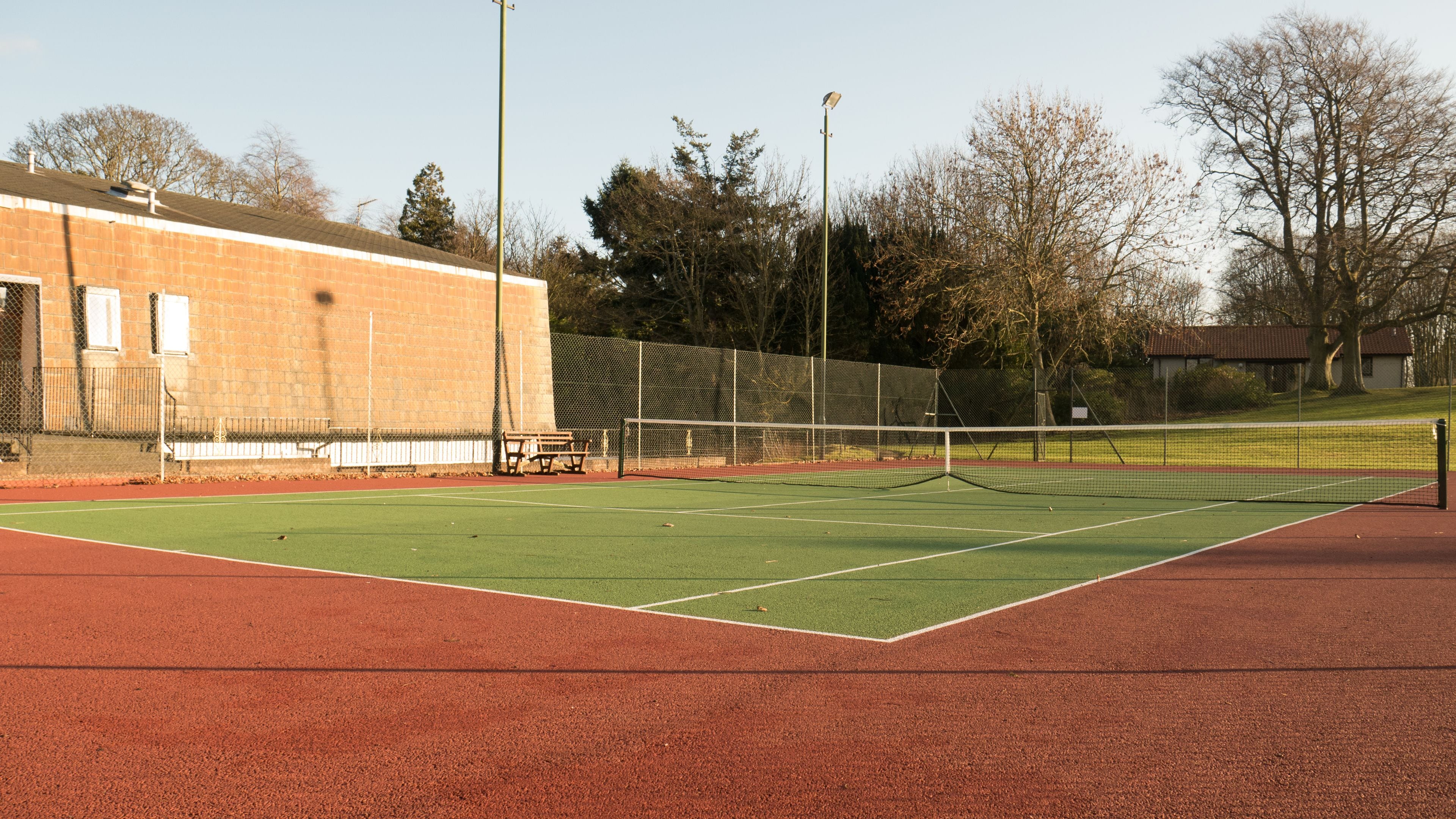 Una cancha de tenis con red, bancos y valla.
