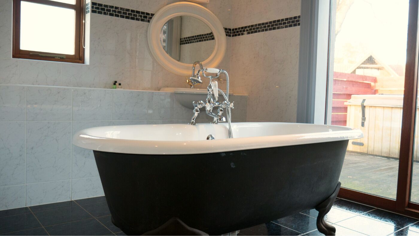 Un baño con una bañera independiente, un espejo y una ventana.