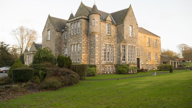 A large stone building with multiple towers and windows, surrounded by a well-maintained lawn and trees. - Kilconquhar Castle Estate (Leven)