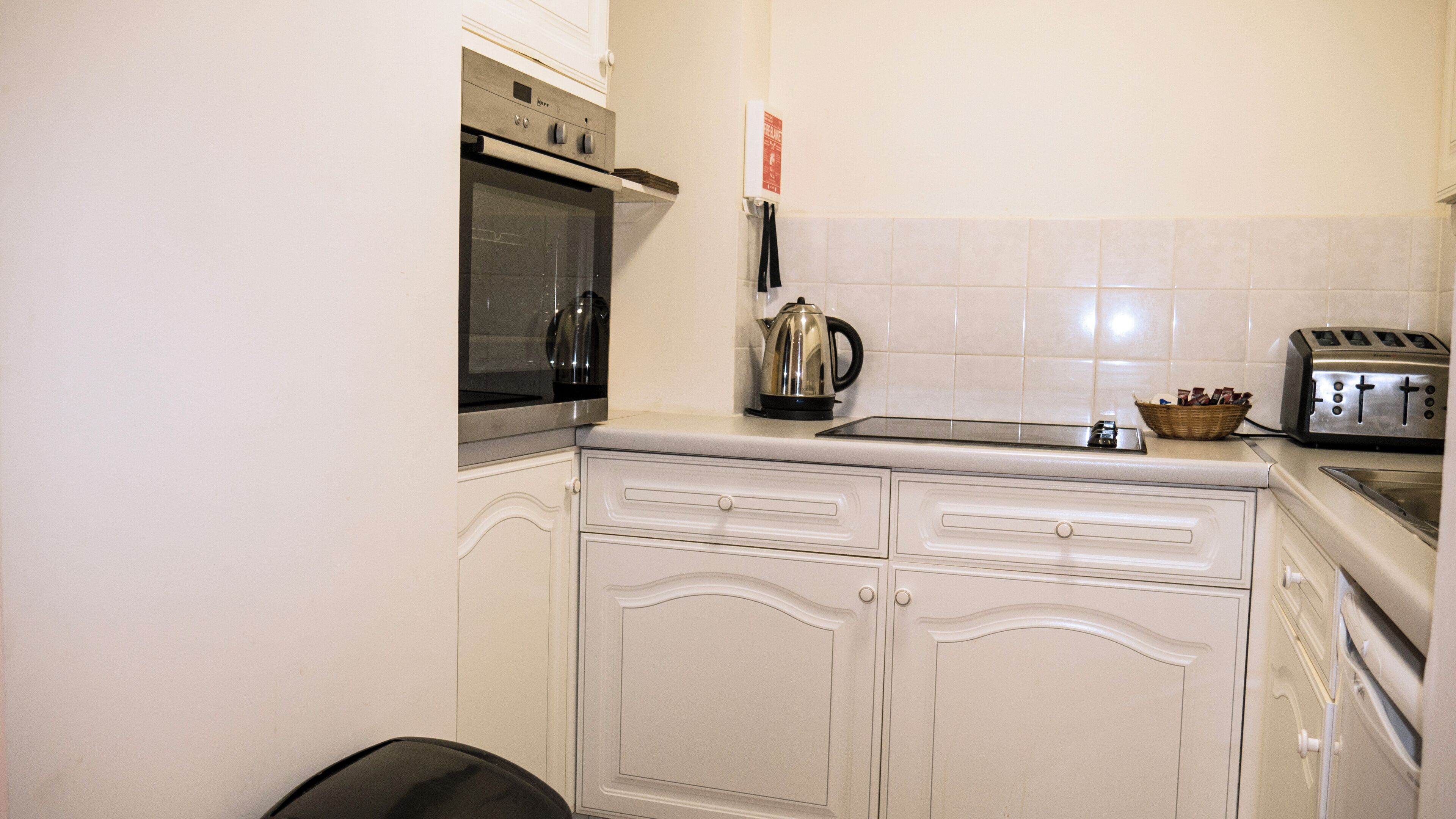 A kitchen with white cabinets, a stainless steel oven, a kettle, a toaster, and a basket of bread.