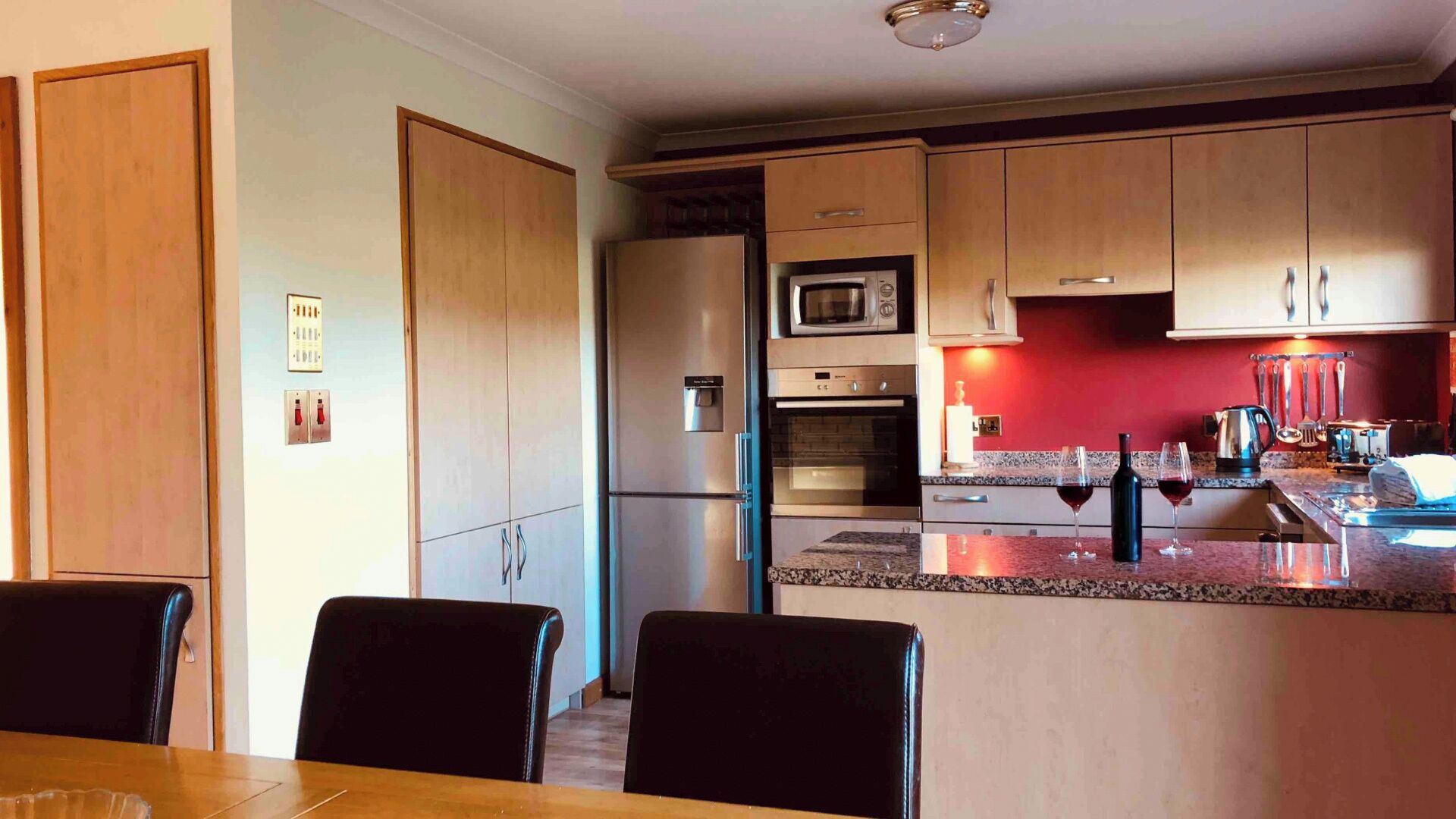 Una cucina moderna con mobili in legno, un frigorifero in acciaio inossidabile, un forno a microonde e una parete di accento rossa.