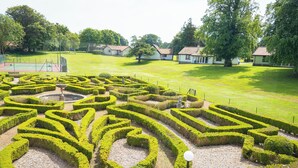 A formal garden with geometric hedge mazes, a central fountain, and traditional buildings in the background. - Kilconquhar Castle Estate (Leven)