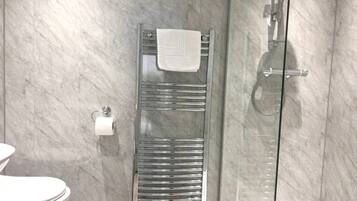 Een moderne badkamer met een douchecabine van glas, een chromen handdoekhouder en een toilet.