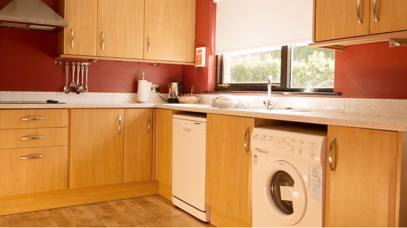 A compact kitchen with wooden cabinets, a dishwasher, and a window providing natural light.
