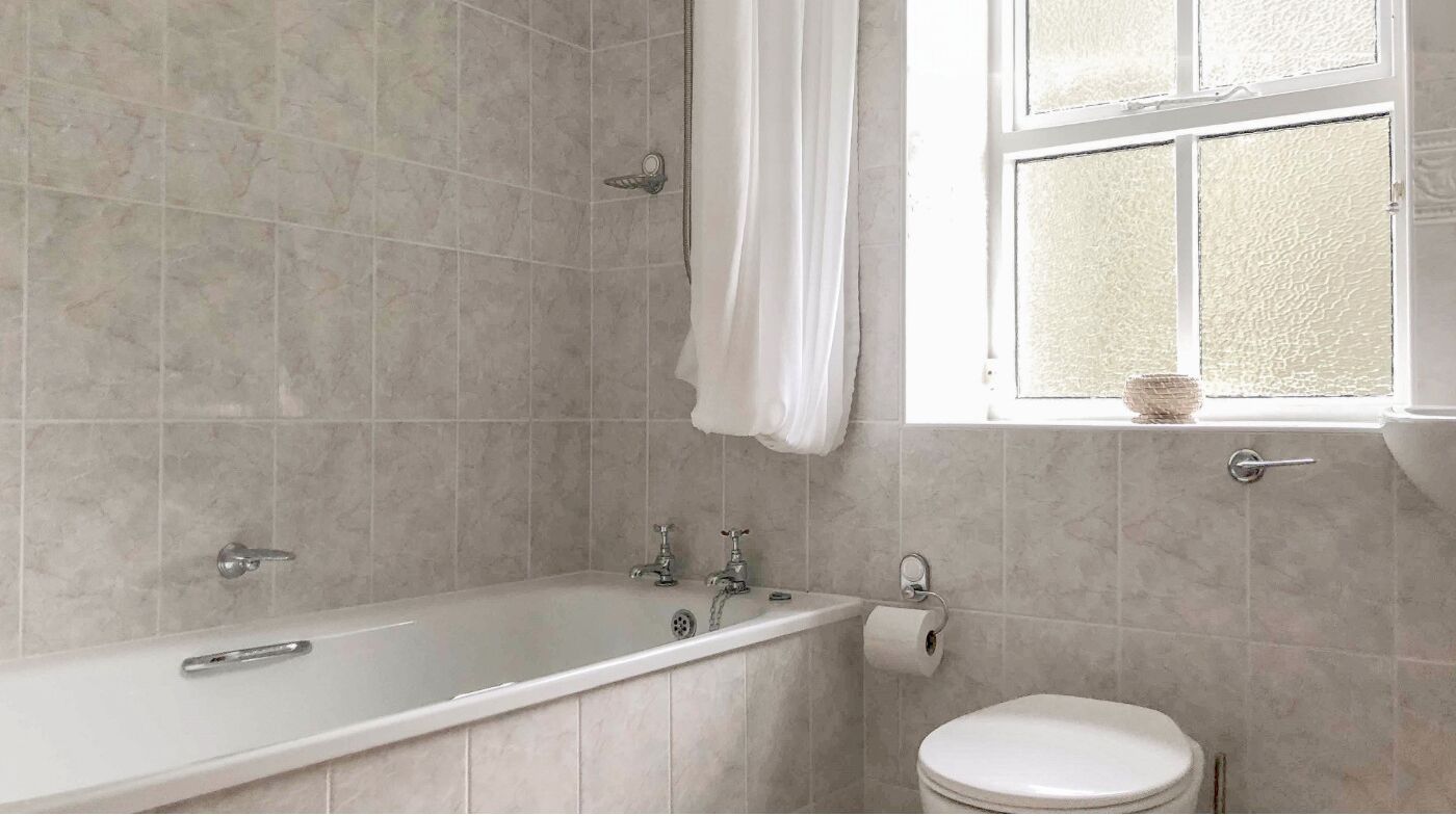 Baño con bañera, inodoro y ventana con cortina.