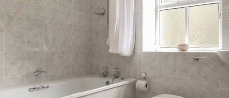 Baño con bañera, inodoro y ventana con cortina.