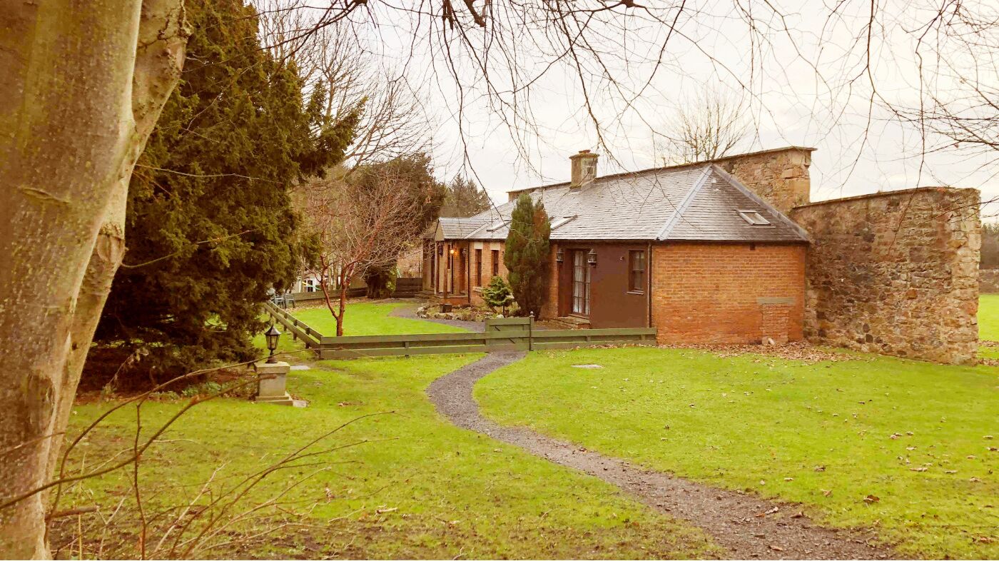 A traditional brick house with a stone wall, a grassy yard, and a winding path leading to the entrance.