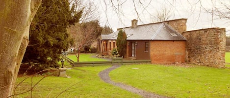 A traditional brick house with a stone wall, a grassy yard, and a winding path leading to the entrance.