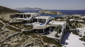 Una villa moderna con piscina, rodeada de terreno rocoso y vistas al mar.