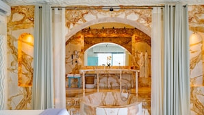 Un baño lujoso con piso de mármol, una bañera central y un tocador con espejo.