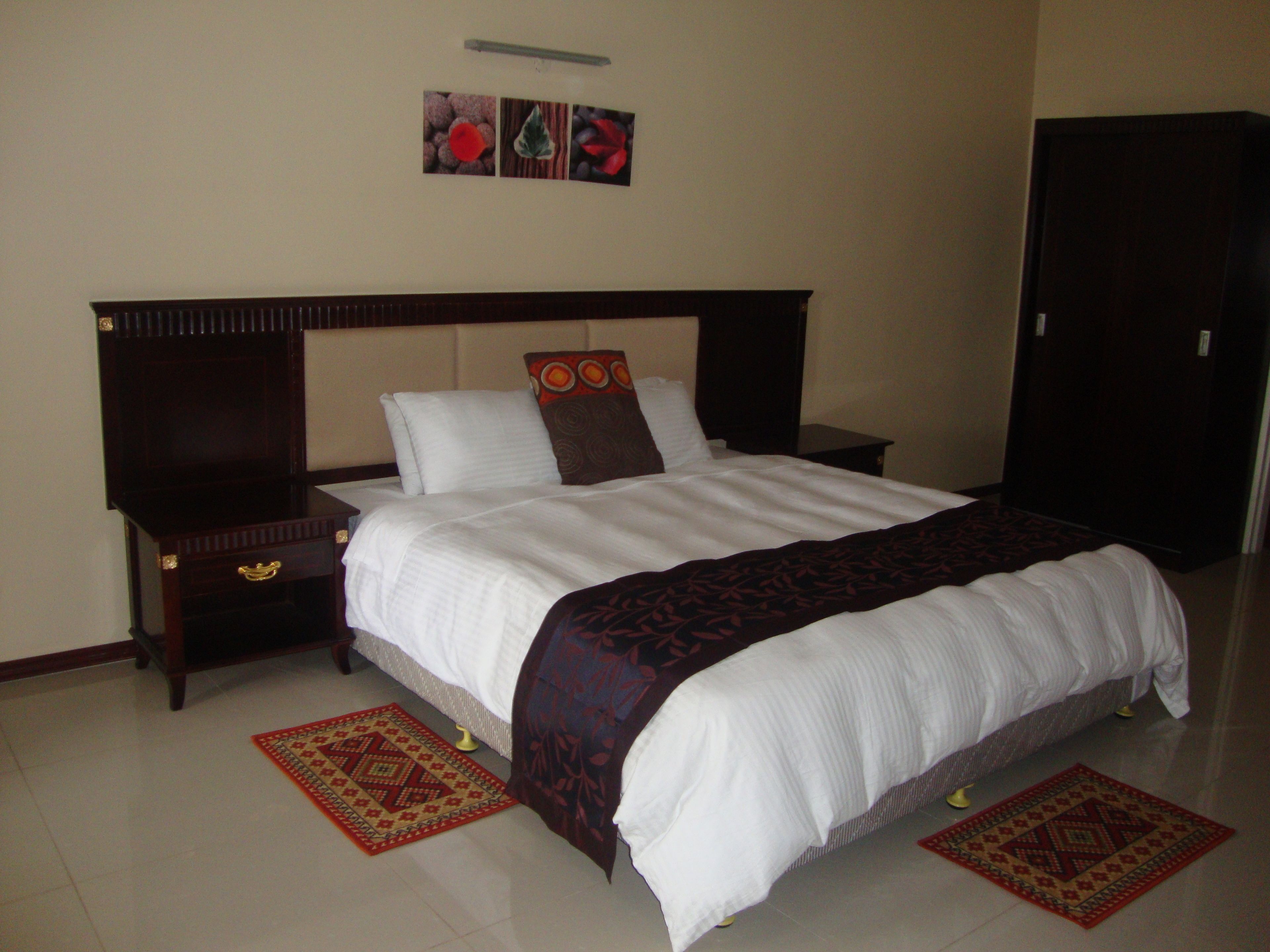 A neatly made bed with a white comforter and a patterned throw blanket, flanked by two nightstands with drawers and a bedside table.