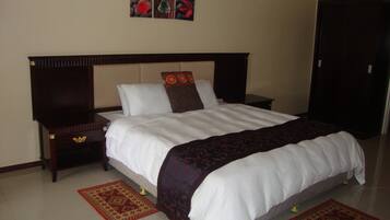 A neatly made bed with a white comforter and a patterned throw blanket, flanked by two nightstands with drawers and a bedside table.