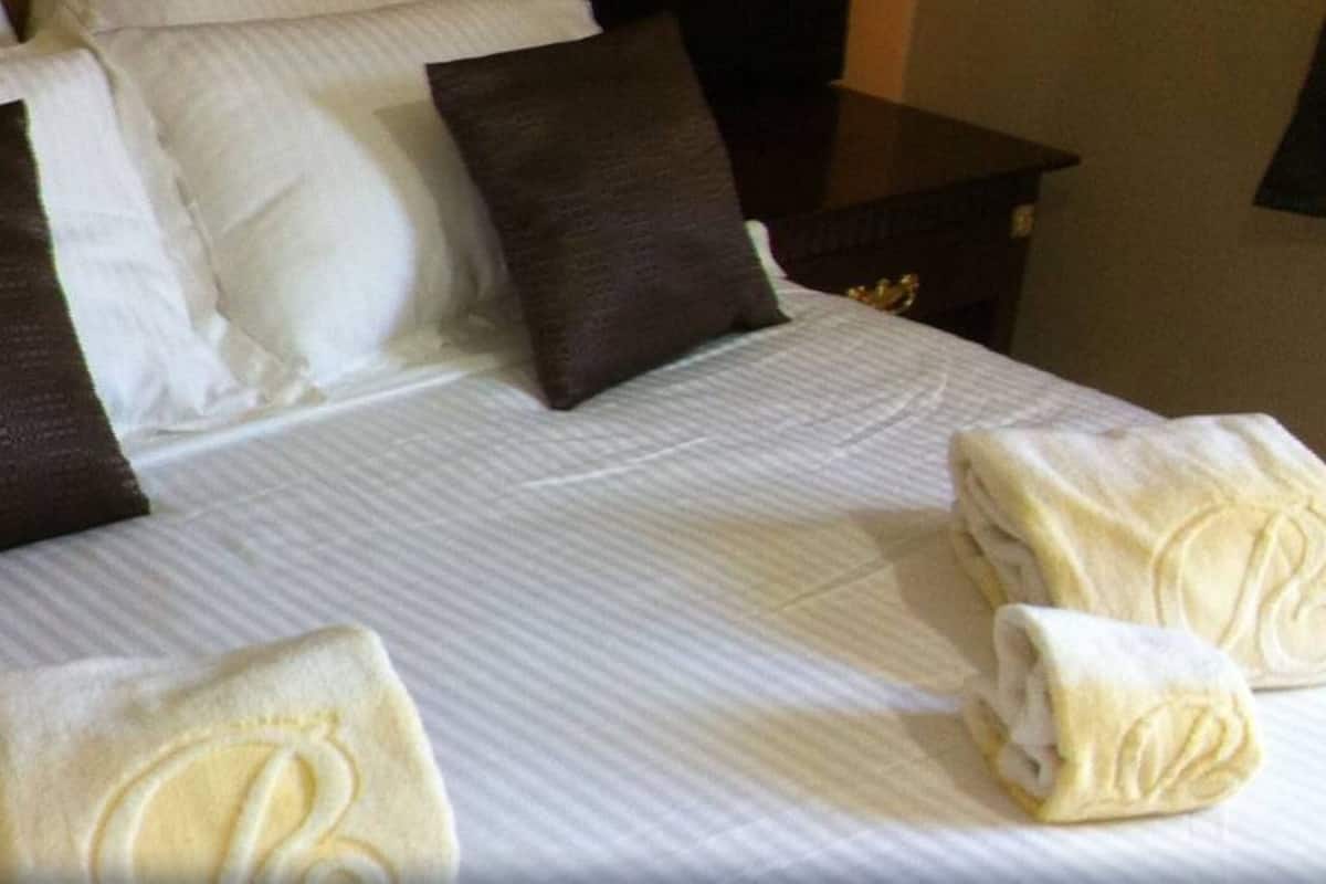 Un lit bien fait, avec des oreillers blancs et bruns, une couvre-lit à rayures et deux serviettes ornées d’un monogramme.