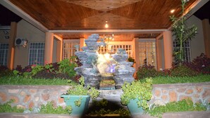 A stone fountain with water spouts, surrounded by potted plants, under a wooden ceiling. - Riverside Hotel and Conference Centre (Lilongwe)