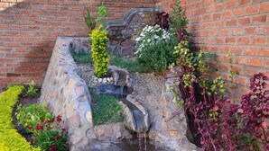 A stone water feature with a small waterfall, surrounded by various plants and flowers. - Riverside Hotel and Conference Centre (Lilongwe)