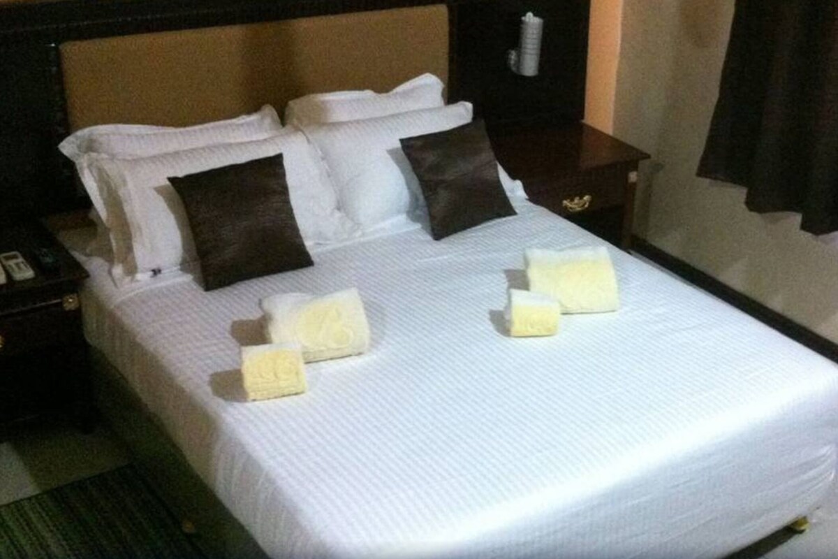 A hotel room with a bed, pillows, a nightstand, and a curtain.