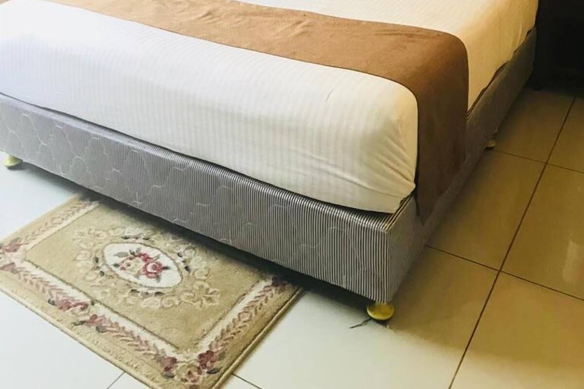 Un lit bien fait, avec une tête de lit marron, du linge de lit blanc et un tapis décoratif.