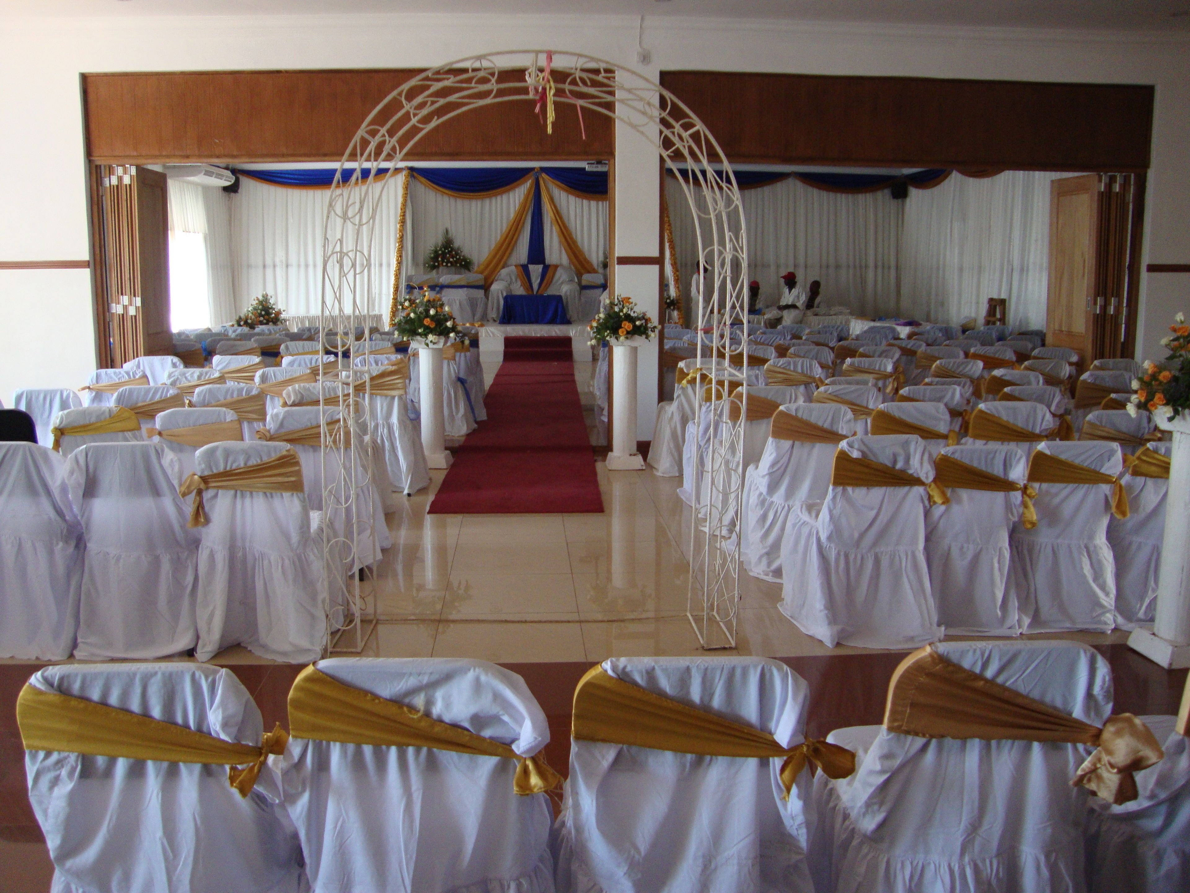 A church interior with rows of pews, a red carpet aisle, and a white archway.