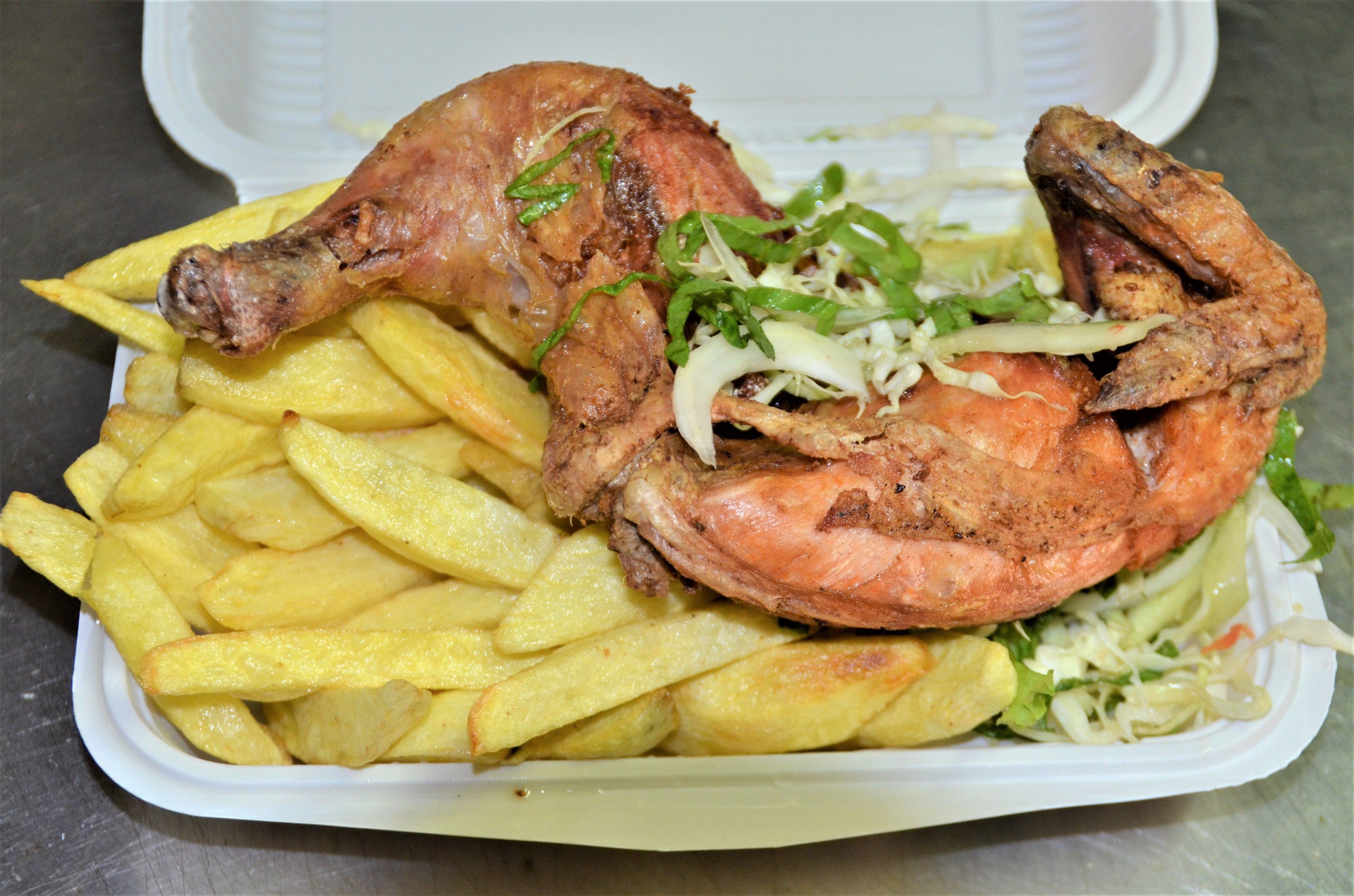 A meal consisting of a roasted leg of lamb, shrimp, and French fries in a takeout container.