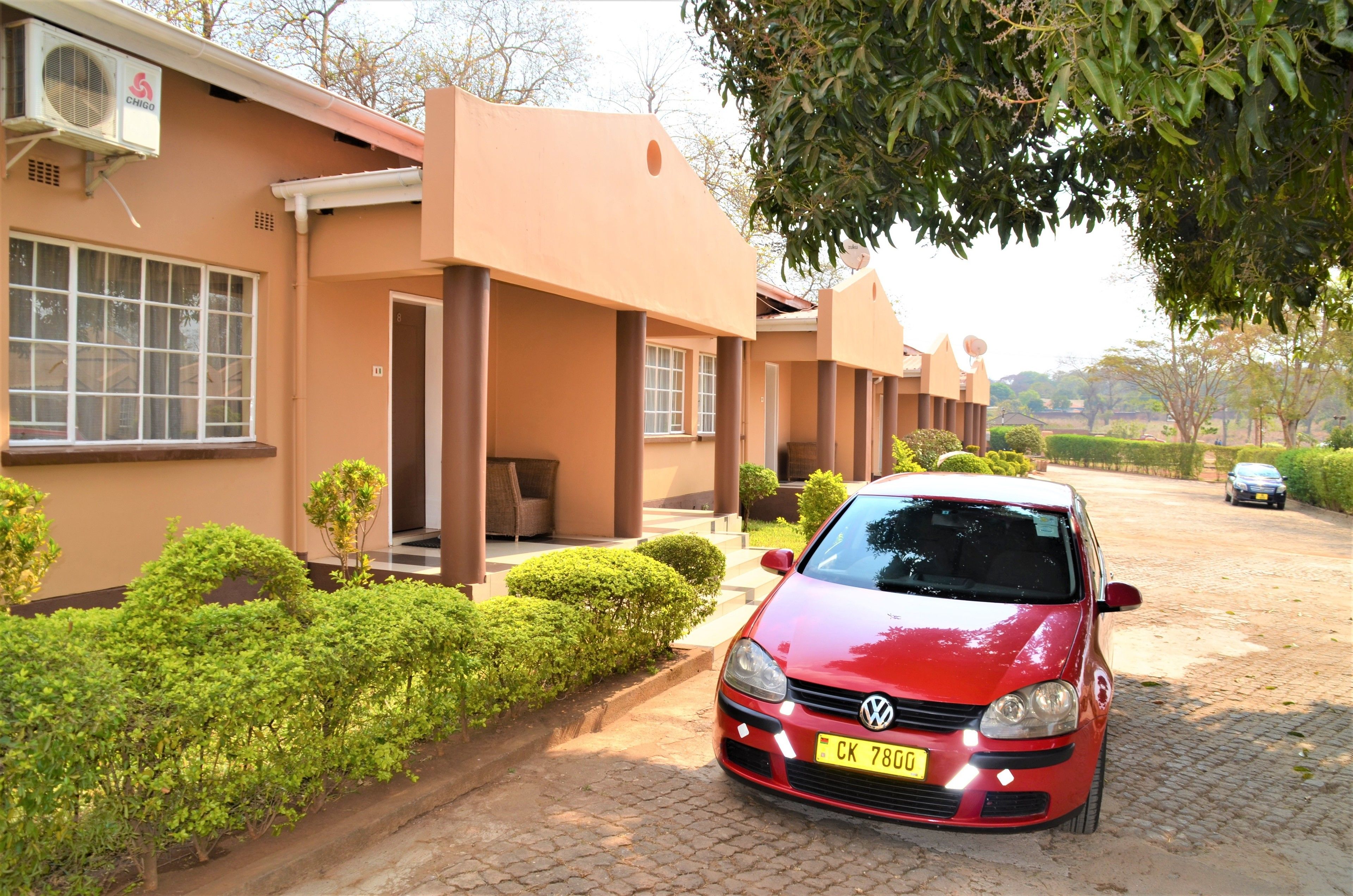 A red Volkswagen parked in front of a building with a beige exterior and a satellite dish.