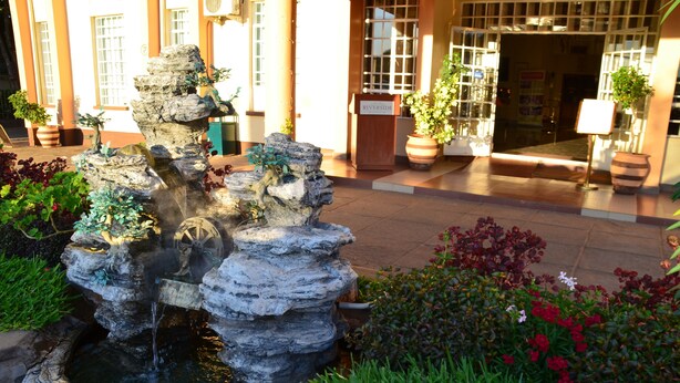 A rock fountain with water cascading down, surrounded by lush greenery and potted plants. - Riverside Hotel and Conference Centre (Lilongwe)