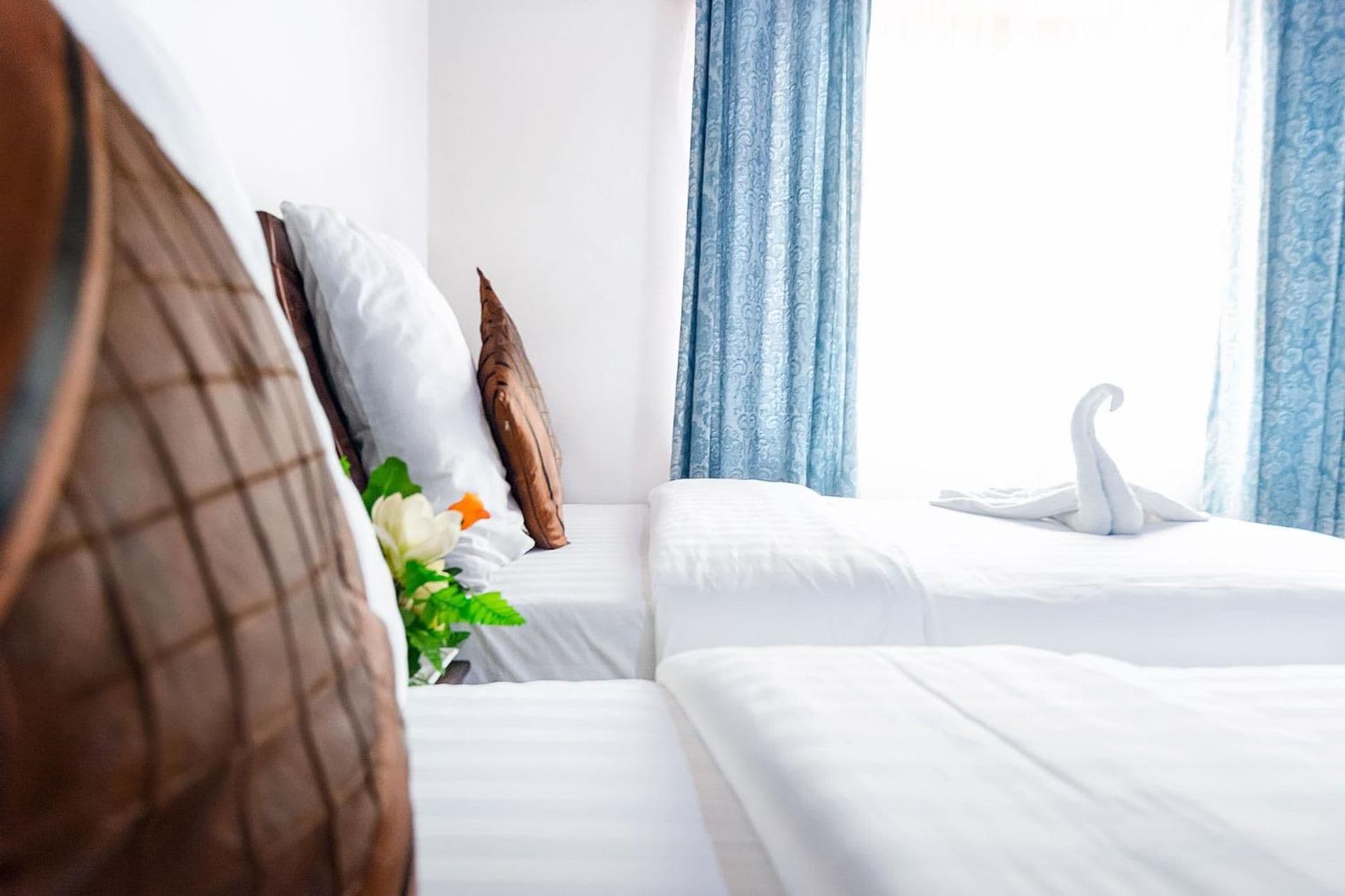 Habitación de hotel con dos camas, ropa de cama blanca, una decoración con forma de cisne en la cama derecha y cortinas azules.
