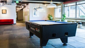 A pool table in a room with a red couch, potted plants, and a window with a view of a building. - WOW Hostel Amsterdam (Amsterdam)
