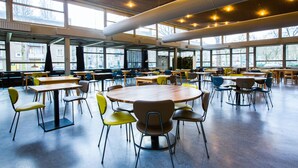 A spacious indoor dining area with multiple tables and chairs, large windows, and a high ceiling with exposed beams. - WOW Hostel Amsterdam (Amsterdam)